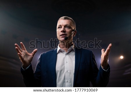 Portrait of men speaking through a microphone in dark conference hall. Person says about marketing and management for successful sales to college students indoors closeup. Professional ideas, politics Royalty-Free Stock Photo #1777910069