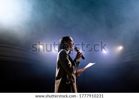 The female financial coach emotional gesturing talks from the stage with spectators at forum. Too many anonymous persons workers and students seat in large auditorium and watch workshop background Royalty-Free Stock Photo #1777910231