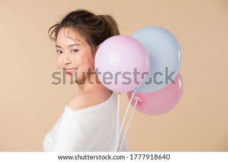 Young Asian girl holding balloons isolated image on light brown background