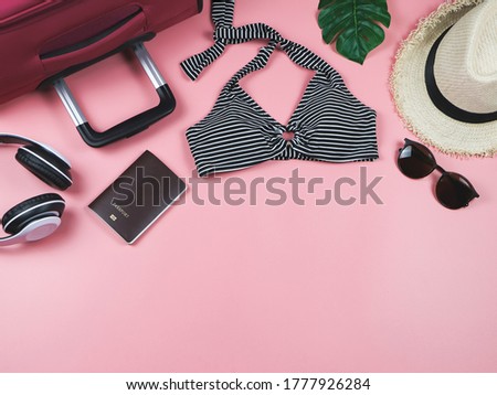 Travel and summer holiday concept, top view of  black and white stripe pattern  bikini swimsuit , passport and women's vacation accessories items  on pink background with tropical monstera leaves.