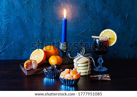 Christmas time, winter, mulled wine in glass, cinnamon, orange and mandarin, cookies and chocolate, a candle in a candlestick.