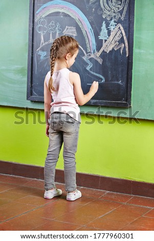 Girl in kindergarten draws on a blackboard with colorful chalk