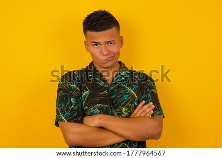 Picture of angry young handsome man crossing arms standing isolated over yellow background. Looking at camera with disappointed expression.