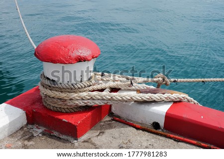 Marine bollard and old rope in pier used for mooring commercial fishing boats and footpath color red and white Is a traffic symbol is that all types of cars are prohibited to stop in this area.