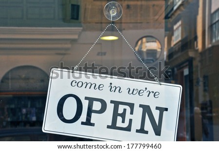 A monochromatic 'Open' sign, in bold black lettering against a pristine white background, gracefully dangles from the door of a charming street cafe.