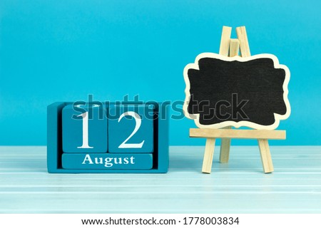 wooden calendar with the date of August 12 and an easel on a blue background, place for text, World Elephant Day, International Youth Day