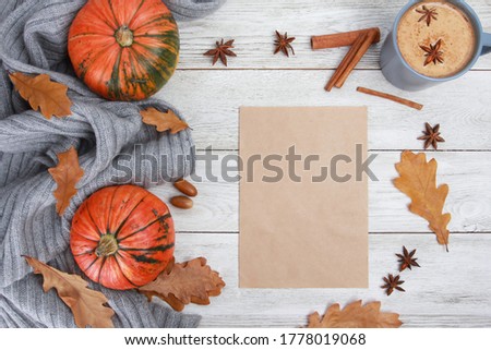 Spicy coffee with milk, grey plaid, spices, dry oak leaves, acorns, orange pumpkins, blank craft paper on white wooden table. Autumn drink concept. Fall, pumpkin latte, thanksgiving, top, copy space