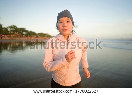 Asian girl running on the beach - young attractive and happy Korean woman doing jogging workout at beautiful beach enjoying fitness and healthy runner lifestyle
