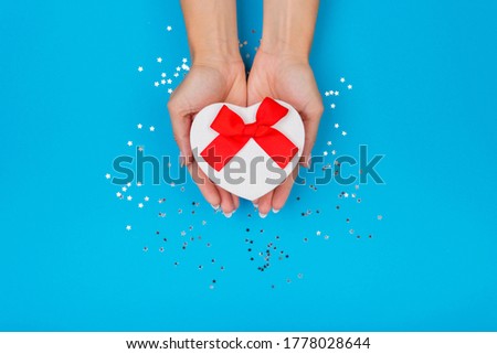 Women hands holding a gift or gift box decorated with confetti on a blue table top view. Flat composition for birthday or wedding.