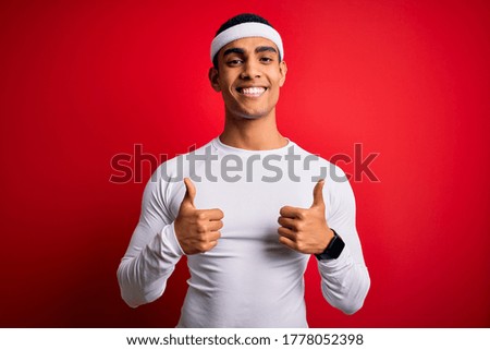 Young handsome african american sportsman wearing sportswear over red background success sign doing positive gesture with hand, thumbs up smiling and happy. Cheerful expression and winner gesture.