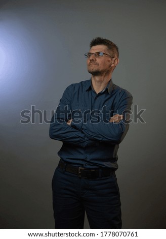 proud guy in grey shirt and denim jeans crosses hands and poses for photo shoot in studio at audition close view