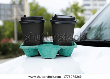 Two glasses of coffee in a stand on a blurred background of the city. Take-out coffee in disposable cups. A quick snack. Coffee cups on the car.