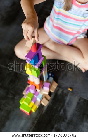 The child plays with a wooden color constructor. The multi-colored details are easy to play. Hands in the photo.