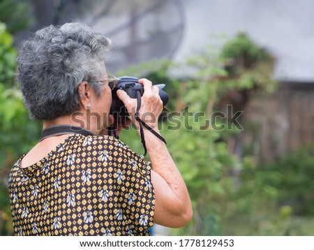 Elderly woman shooting photo by digital camera at garden. Asian senior woman short white hair, wearing eyeglasses, happy when using a camera. Concept of old people and photography