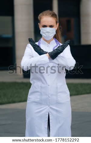 A portrait of a doctor's girlfriend in a medical mask and a woman holding her hands in front of her in a stop sign. The concept of protection