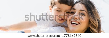 panoramic concept of cheerful mother looking at camera near adorable son