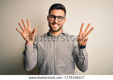 Young handsome man wearing elegant shirt and glasses over isolated white background showing and pointing up with fingers number eight while smiling confident and happy.