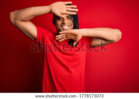 Young handsome african american afro man with dreadlocks wearing red casual t-shirt Smiling cheerful playing peek a boo with hands showing face. Surprised and exited