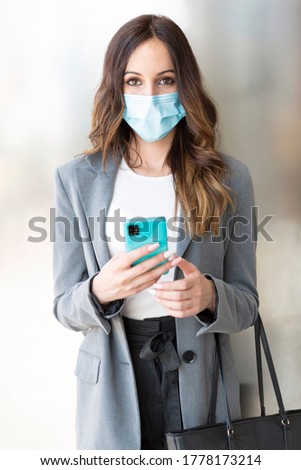 Vertical portrait of a businesswoman in formal clothes. She is wearing a medical mask and has a smartphone in her hand. Selective focus. Business and new normal concept. 