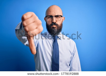 Handsome business bald man with beard wearing elegant tie and glasses over blue background looking unhappy and angry showing rejection and negative with thumbs down gesture. Bad expression.