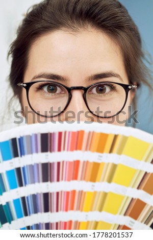 Young woman portrait, wearing glasses with color palette, close up portrait, only eyes are visible. Female model holding pantone chart.