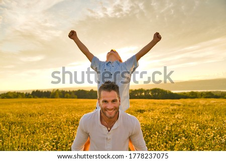 A happy family of father and child on field at the sunset having fun on back with hand high