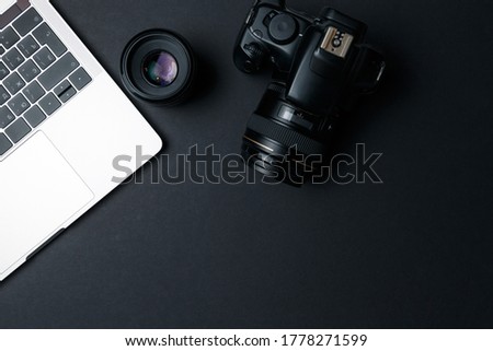Photographer's workplace on a dark background. Modern laptop, digital camera, lens, battery, smartphone. Minimalism. Top view. Copy space. Equipment for the photographer. The concept of freelancing