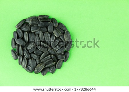 Round pile of roasted sunflower seeds on green paper background. Cope space for text.