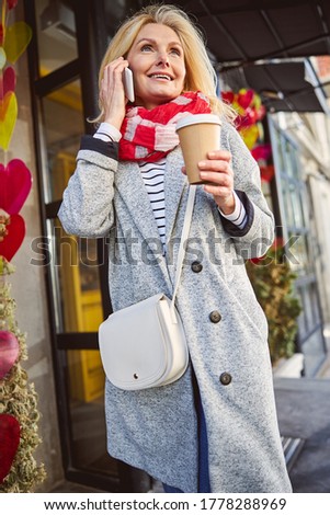 Happy pretty woman using smartphone and holding takeaway coffee with terrace on the background