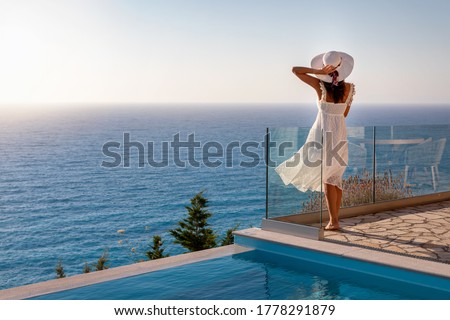 A elegant luxury woman in a white dress enjoys the summer sunset by the pool overlooking the Aegean Sea in Greece Royalty-Free Stock Photo #1778291879
