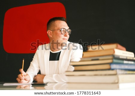 A young school teacher a man in a white jacket and glasses checks the homework of his students and prepare for a new lesson. Education, school, college and university concept.