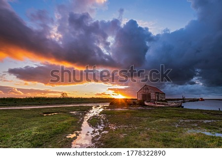 Setting sun on horizon with derelict boat and boat house in forground