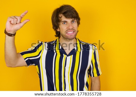 Blond European man over isolated background gesturing with hand showing small size, measure symbol. Smiling looking at the camera. Measuring concept.