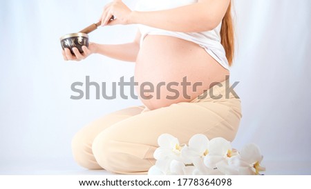 Pregnant woman practicing breathing prenatal exercises with beautiful flowers orchids on white background. Relaxation and delivery preparation mindfulness concepts. Sports concept.