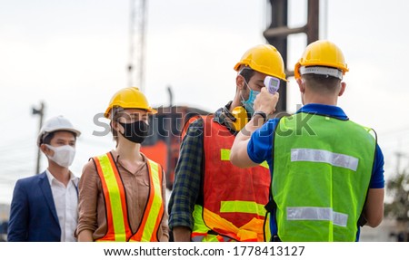 Factory worker man checking fever by digital thermometer for scan and protect from Coronavirus (COVID-19) at cargo containers - Healthcare Concept Royalty-Free Stock Photo #1778413127