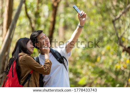 Tourist and traveler asian couple backpack enjoy happy take a photo selfie in the jungle forest nature park . Traveler going camping and explore outdoors destination leisure.