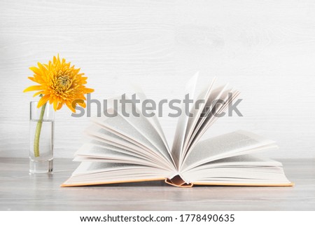 The concept of international knowledge day, teacher's day, and education. On the table is an open book, next to it a yellow flower in a vase.
