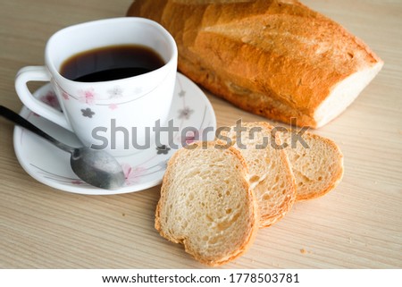 French bread cut into pieces, placed beside a white coffee mug on a light wooden table where the crumb stuck.