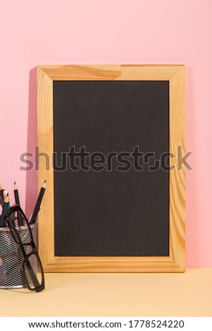 Chalkboard, books, glasses and pens on yellow pink background. Concept to teacher's day. Copy space.