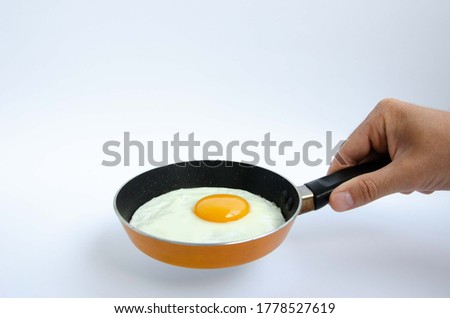 A man holds a small frying pan with freshly fried egg. Frying pan in a man's hand and scrambled eggs. Royalty-Free Stock Photo #1778527619