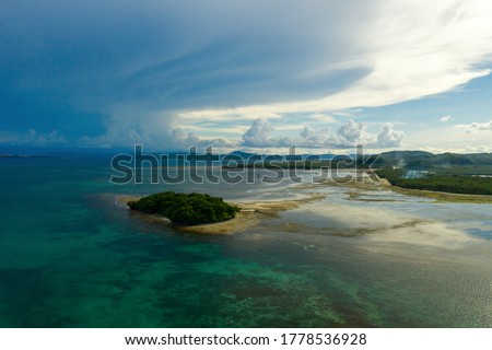 Drone picture of turtle island in low tide near siargao island, philippines, its beach, malinao beach on the right side, and a cloudy grey sky in the background