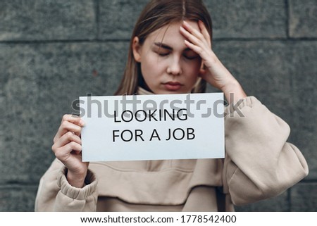 Young woman hold white paper poster in hand. Sad Girl with white blank template sheet with inscription Looking for a job