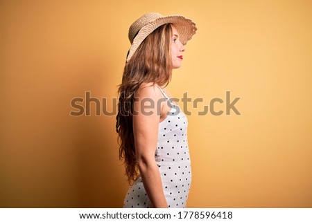Young beautiful blonde woman on vacation wearing summer hat over yellow background looking to side, relax profile pose with natural face with confident smile.