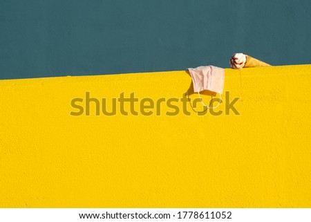 Covid-19 mask with ice cream with a cone melting in summer with the heat of the sun on a yellow and blue background. Holiday and coronavirus concept