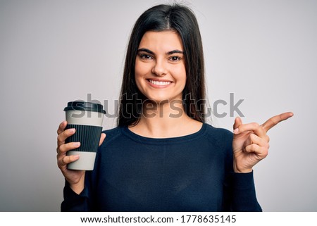 Young beautiful brunette woman drinking cup of coffee over isolated white background very happy pointing with hand and finger to the side