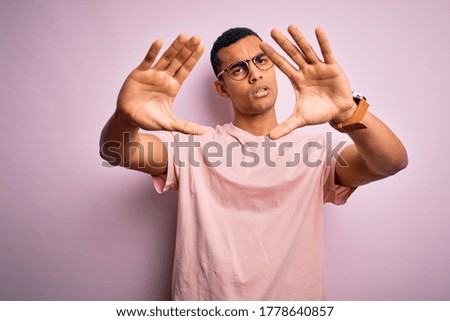 Handsome african american man wearing casual t-shirt and glasses over pink background doing frame using hands palms and fingers, camera perspective
