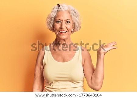 Senior grey-haired woman wearing casual clothes smiling cheerful presenting and pointing with palm of hand looking at the camera. 