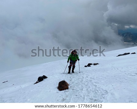 Climber with a backpack and trekking poles walks along a snowy path. Beautiful mountain winter landscape. Snowy slopes of the northern Elbrus region. Storm. Royalty-Free Stock Photo #1778654612