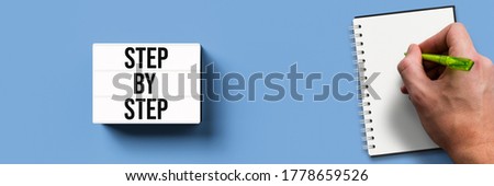 lightbox with message STEP BY STEP and hand with notepad on blue background
