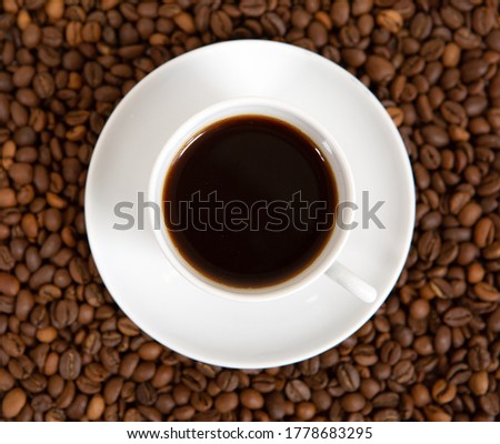 Hot coffee in a Cup and plate stands on a carpet of coffee beans, close-up photo